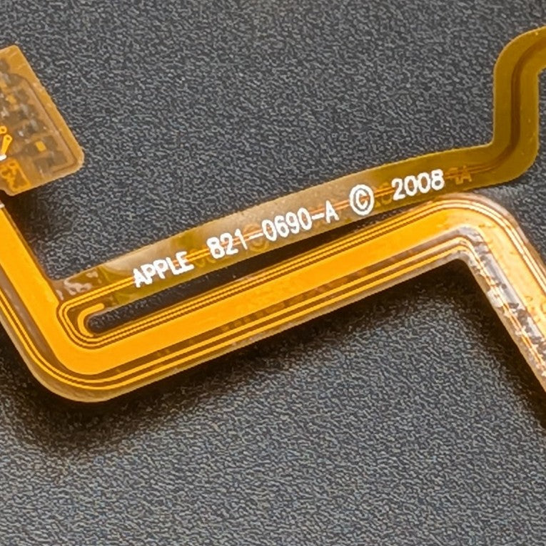 A close-up of a flexible circuitry ribbon cable with white printed text reading 'APPLE 821-0690-A © 2008' on a dark textured background.