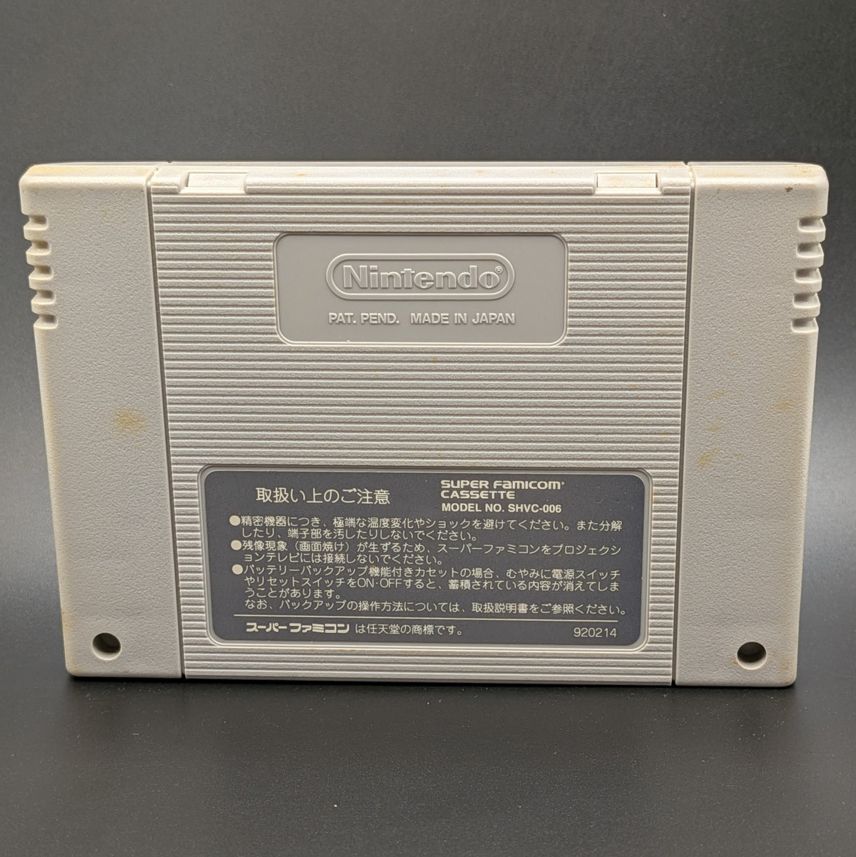 Aguri Suzuki F-1 Super Driving video game cartridge for Nintendo's Super Famicom (SFC) Entertainment System, showing the back of the cart, standing up on a dark grey background.
