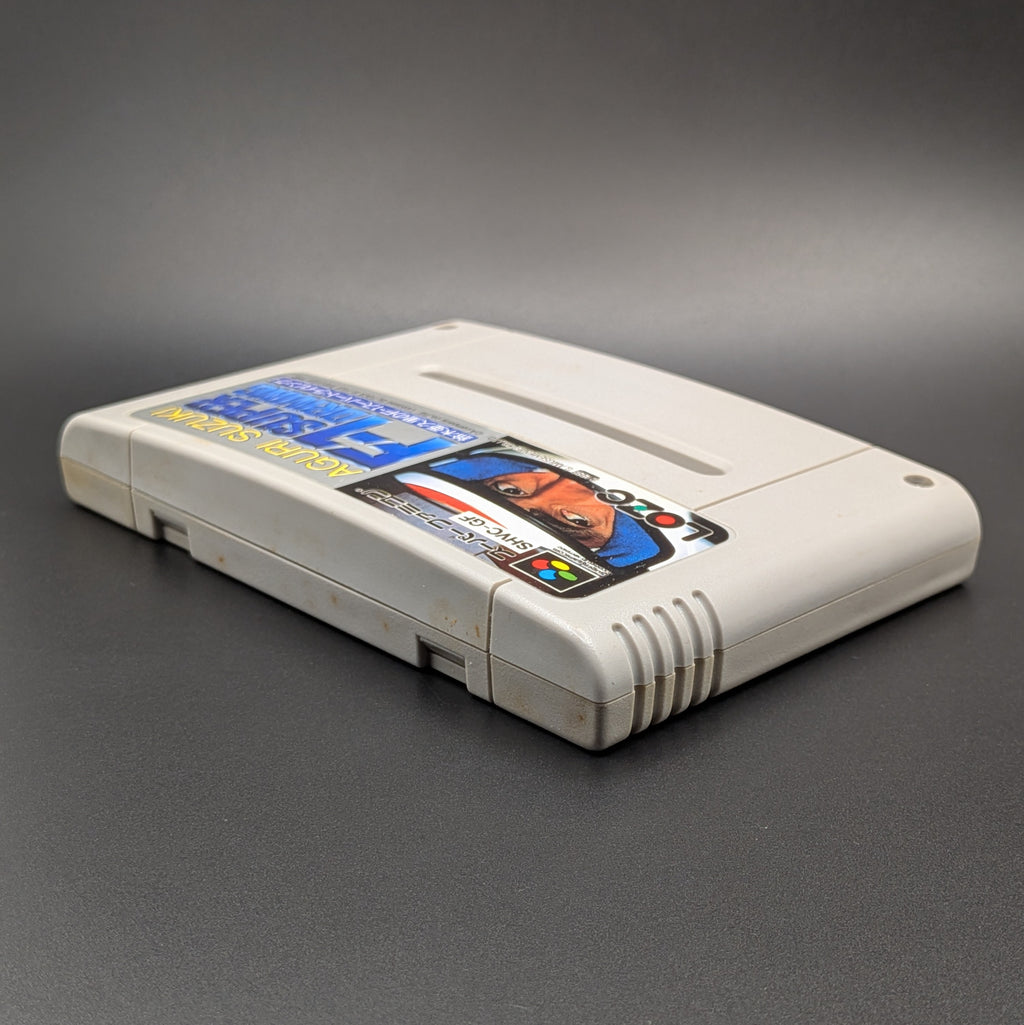 Aguri Suzuki F-1 Super Driving video game cartridge for Nintendo's Super Famicom (SFC) Entertainment System, shown laying on its back, facing upwards showing the front label and top edge, at a 3/4 angle on a dark grey background.
