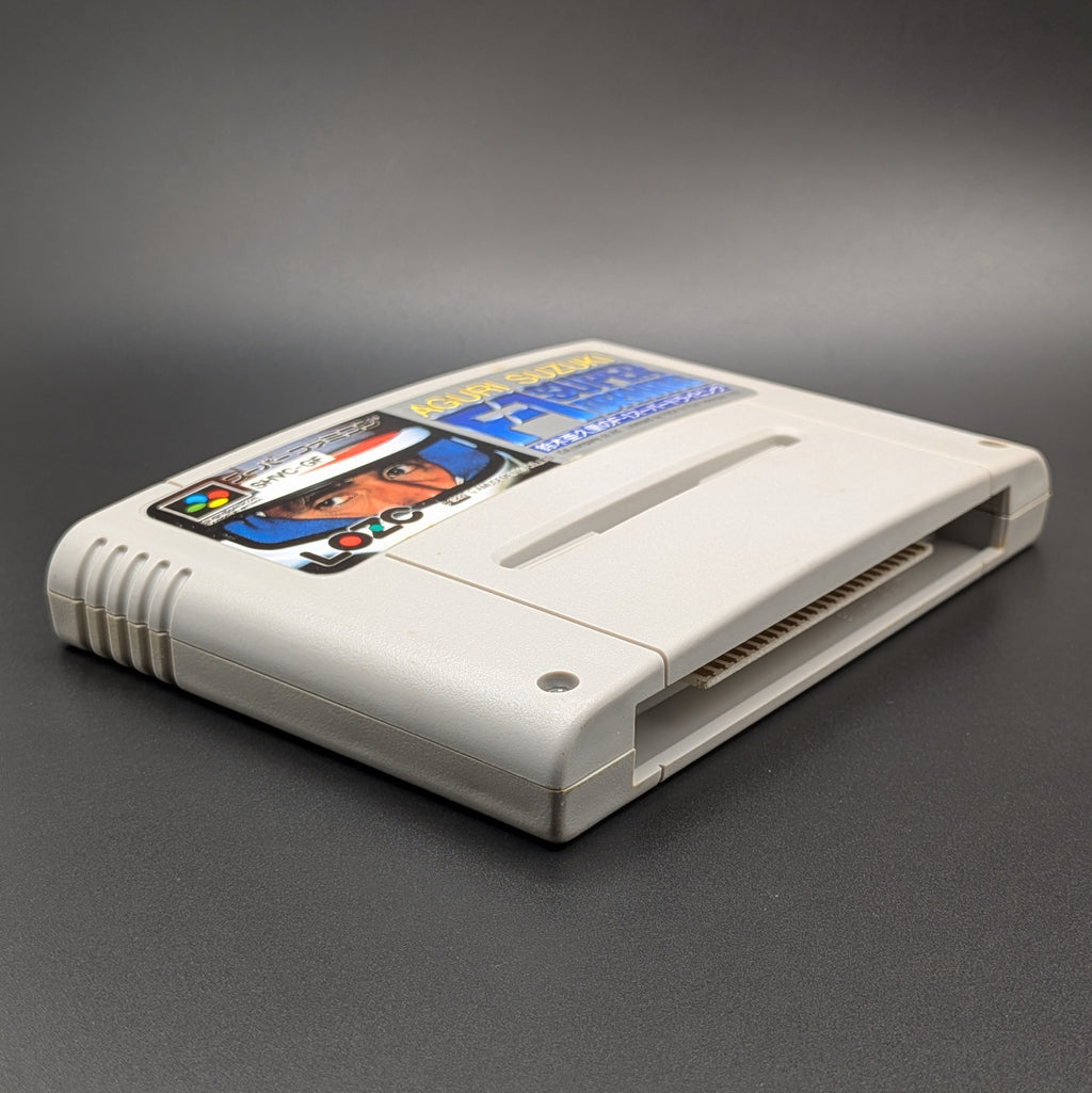 Aguri Suzuki F-1 Super Driving video game cartridge for Nintendo's Super Famicom (SFC) Entertainment System, shown laying on its back and facing upwards showing the front label, at a 3/4 angle on a dark grey background.
