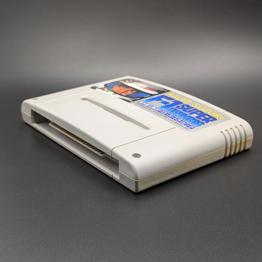 Aguri Suzuki F-1 Super Driving video game cartridge for Nintendo's Super Famicom (SFC) Entertainment System, shown laying on its back, facing upwards showing the front label and bottom edge, at a 3/4 angle on a dark grey background.
