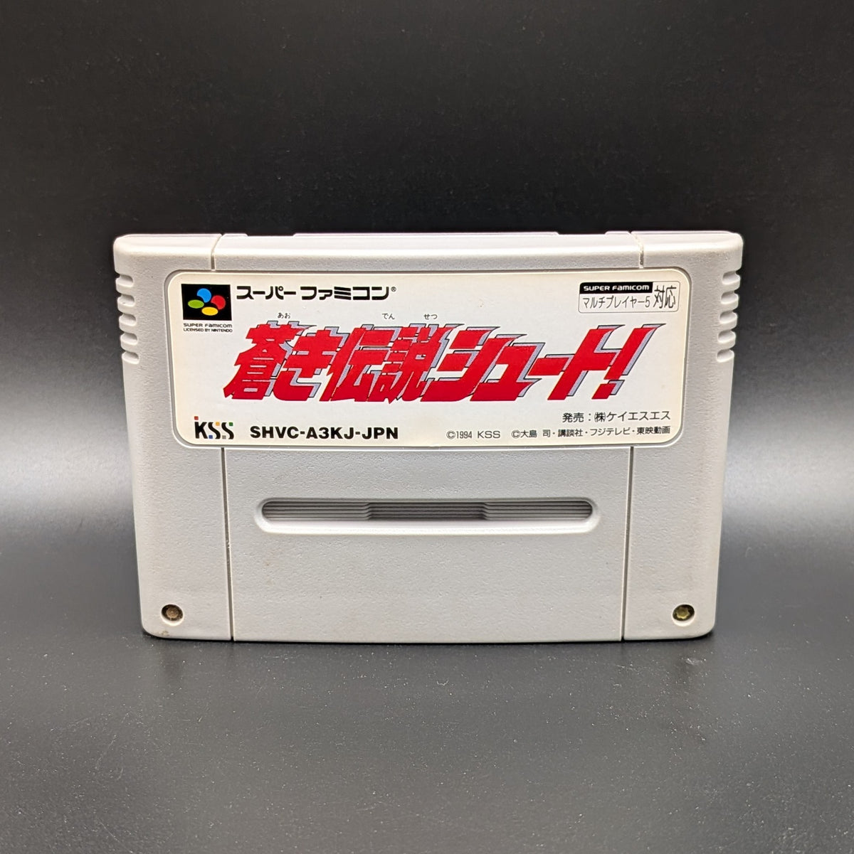 Aoki Densetsu Shoot video game cartridge for Nintendo's Super Famicom (SFC) Entertainment System, shown standing up and facing forward on a dark grey background.
