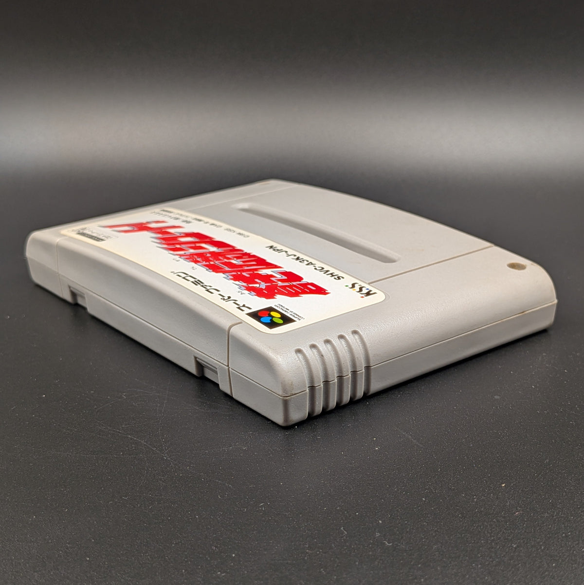 Aoki Densetsu Shoot video game cartridge for Nintendo's Super Famicom (SFC) Entertainment System, shown laying on its back with the label facing upwards. Showing the left hand side and top edge. It sits on a dark grey background.