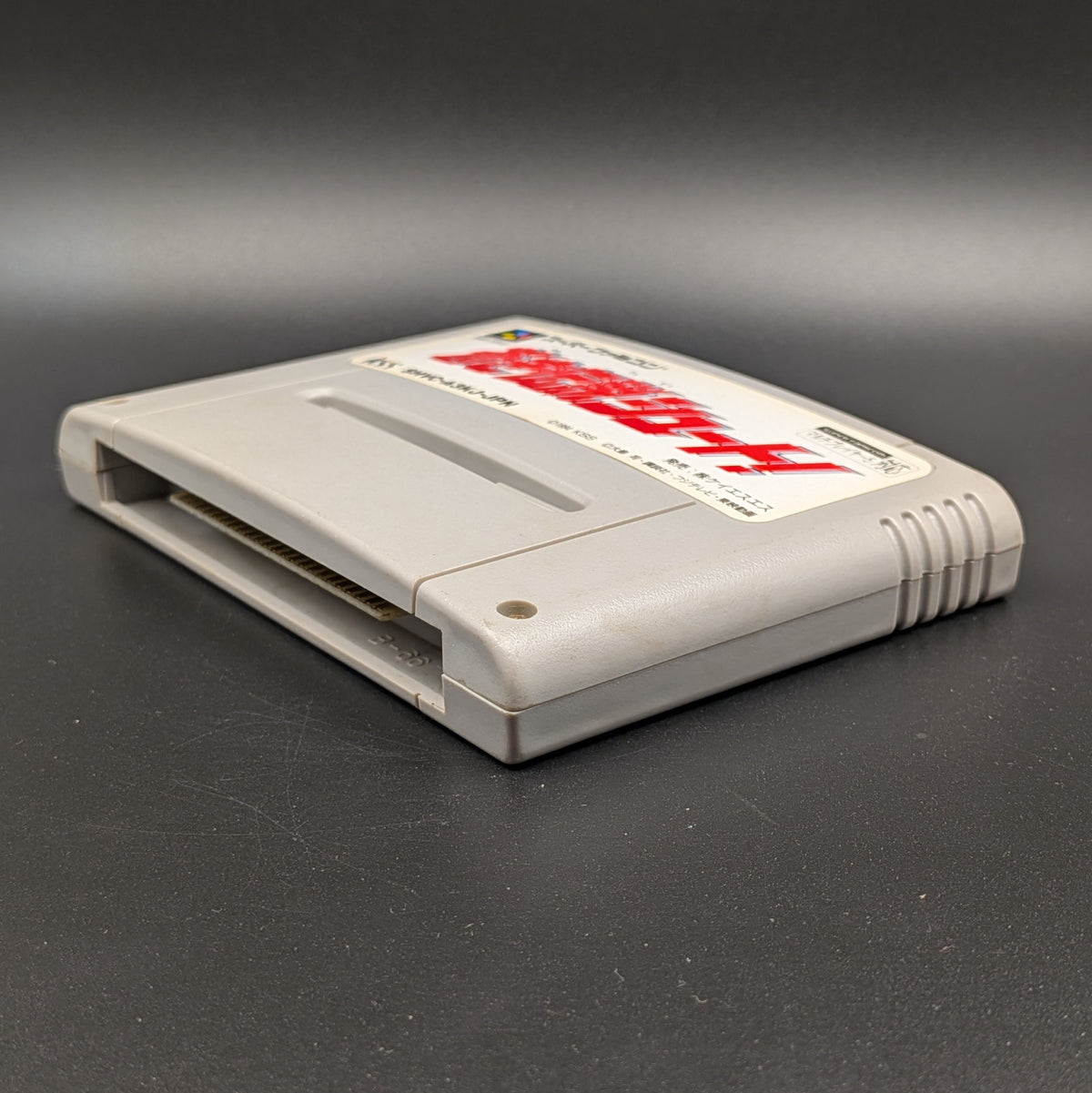 Aoki Densetsu Shoot video game cartridge for Nintendo's Super Famicom (SFC) Entertainment System, shown laying on its back with the label facing upwards. Showing the right hand side and bottom slot. It sits on a dark grey background