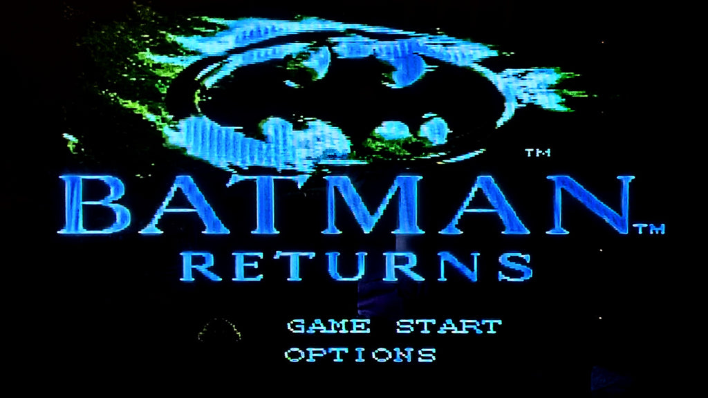 Digital title screen for the video game Batman Returns for the Super Famicom (SFC), featuring the Batman logo in glowing blue above the title 'BATMAN RETURNS' in large blue letters, with 'GAME START' and 'OPTIONS' below on a black background. Taken to show the game is tested and working.