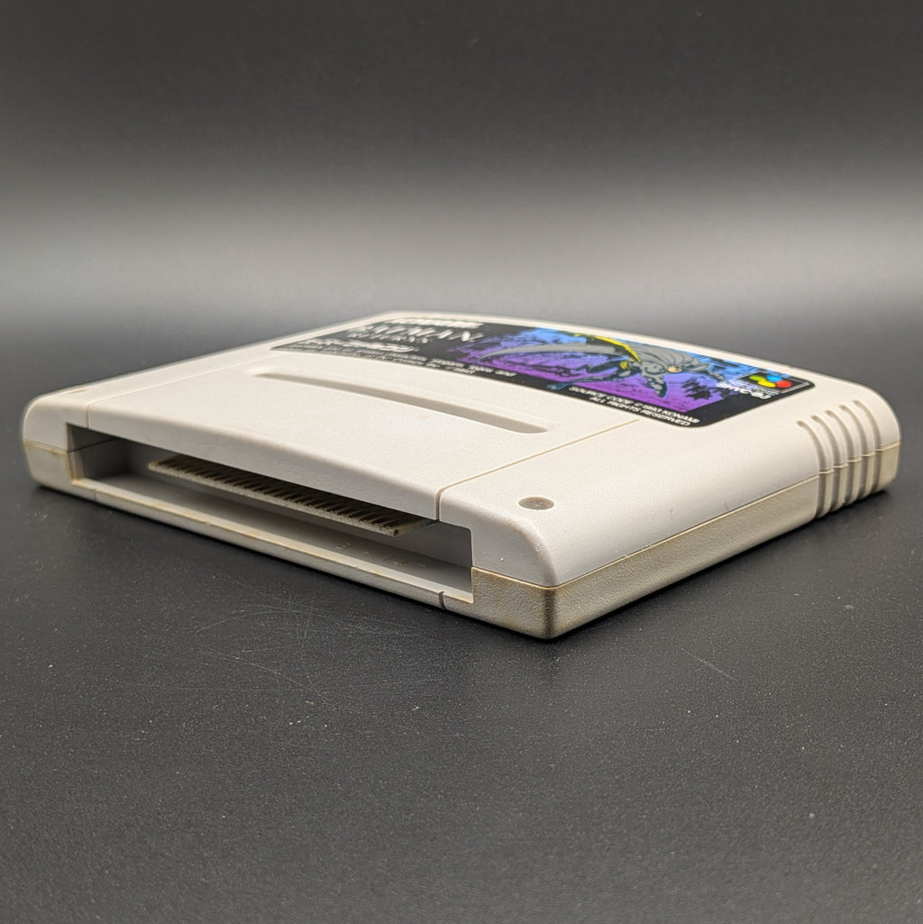 Batman Returns video game cartridge for Nintendo's Super Famicom (SFC) Entertainment System, shown laying on its back with the label facing upwards. Showing the right hand side and bottom slot. It sits on a dark grey background.