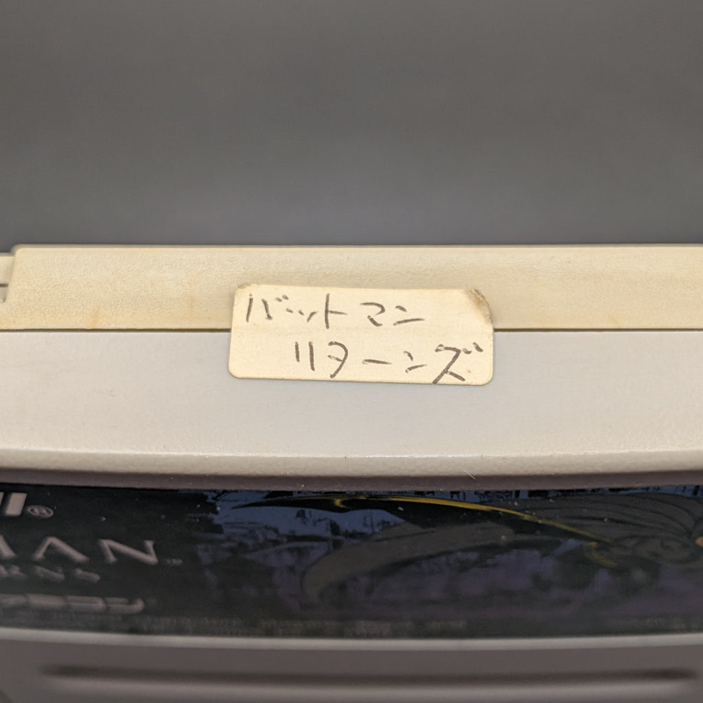 Batman Returns video game cartridge for Nintendo's Super Famicom (SFC) Entertainment System. On the top edge is a small white sticker with Japanese hand writing on it, shown up close.