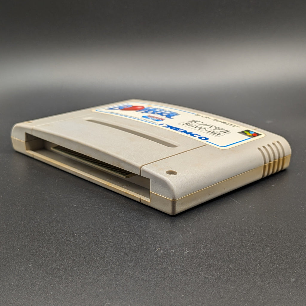 Bombuzal video game cartridge for Nintendo's Super Famicom (SFC) Entertainment System, shown laying on its back with the label facing upwards. Showing the right hand side and bottom slot. It sits on a dark grey background. 
