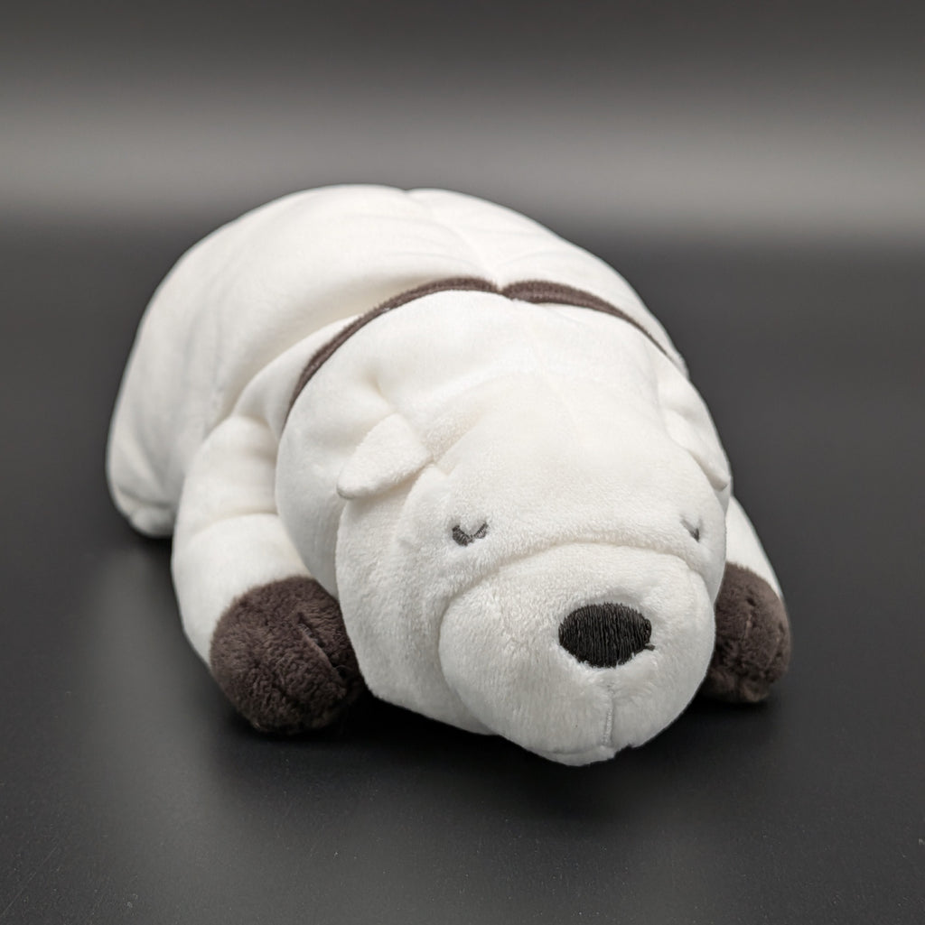 A plush Bond Forger dog toy shown lying on its belly, facing forwards at 3/4 view angle. Sitting on a dark grey surface, with soft white fur and brownish grey accents on its paws, snout, and collar. From the anime/manga series Spy X Family, made by Club Mochi-Mochi.