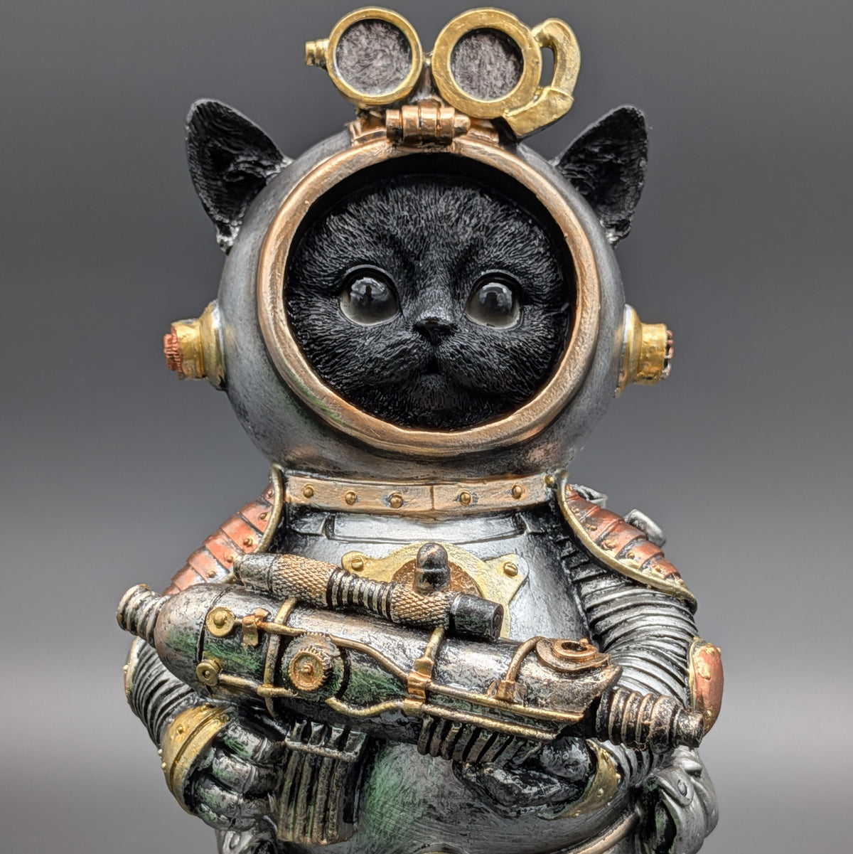 A black cat dressed as a retro sci-fi space explorer in a detailed metallic spacesuit with gold goggles and a gun, set against a solid gray background.