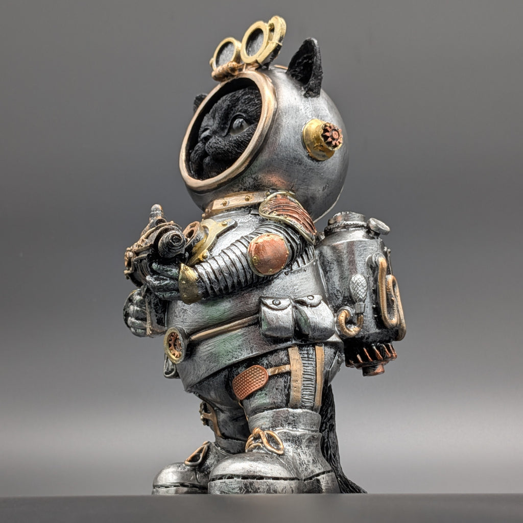 A detailed collectible figurine of a black cat dressed in a vintage, weathered silver and gold space suit, standing against a neutral gray studio background.