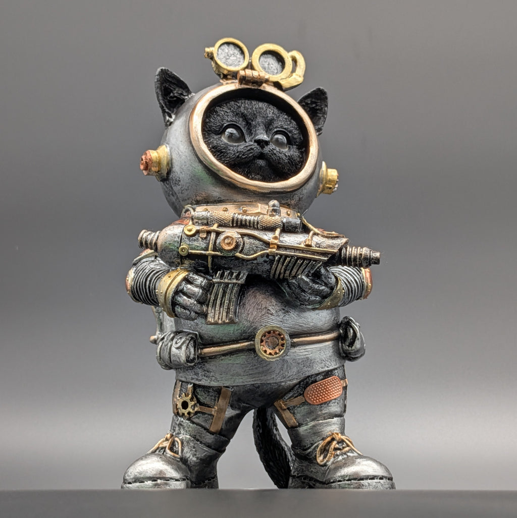 A collectible figurine of a black cat dressed in a detailed steampunk-style metallic gray and gold space suit, holding a futuristic rifle, set against a neutral gray background.