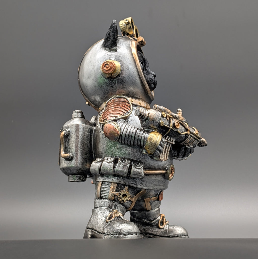 A small decorative figurine of a stylized cat dressed in a detailed, weathered steampunk-style space suit. The suit features rusted copper panels, brass-toned metal accents, and a silver-gray body, set against a neutral gray studio background.