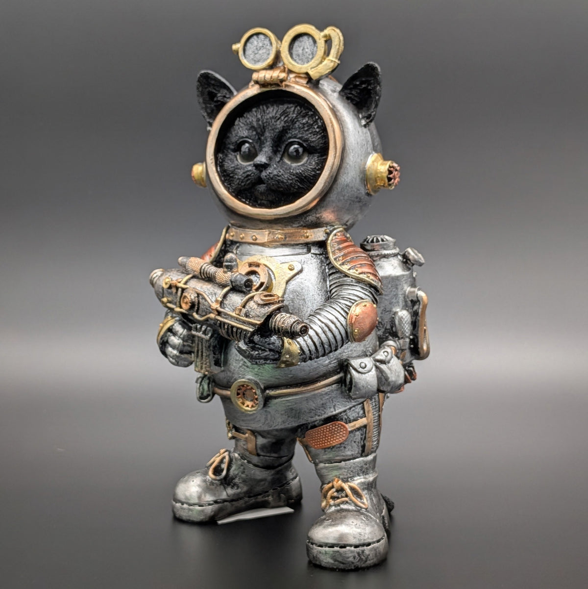A decorative figurine of a black cat dressed in a detailed steampunk-style space suit, standing against a dark gray gradient background.