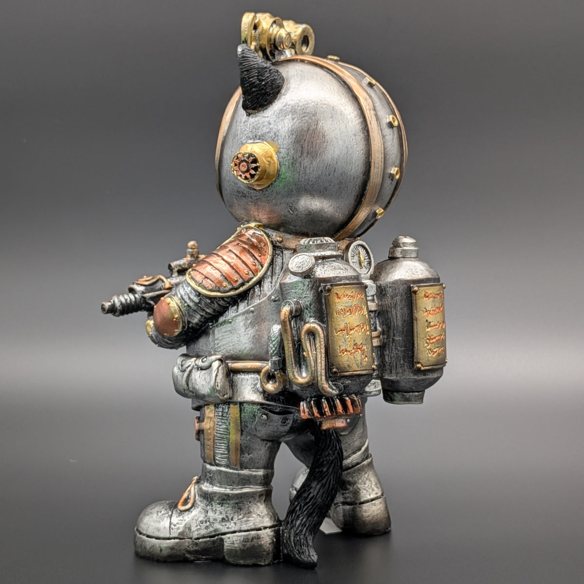 A detailed collectible figurine of a steampunk-style space suit character, featuring a metallic silver helmet, copper and bronze mechanical armor, and a black cat tail, set against a dark gray gradient background.