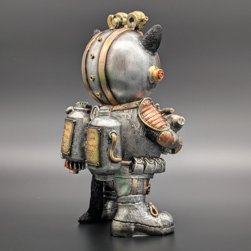 A steampunk-style astronaut cat figurine shown from the back, featuring a metallic silver helmet with gold accents, a detailed silver space suit, and black cat ears and tail, set against a dark gray gradient background.