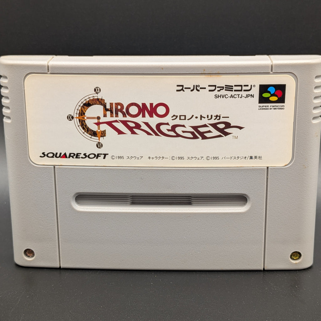 A close up of Chrono Trigger video game cartridge for Nintendo's Super Famicom (SFC) Entertainment System, shown standing up and facing forward on a dark grey background.
