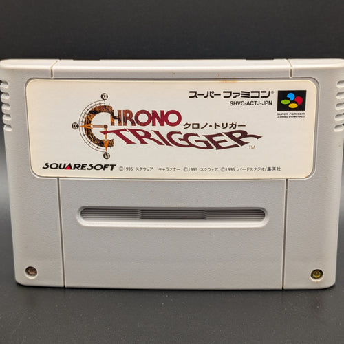 A close up of Chrono Trigger video game cartridge for Nintendo's Super Famicom (SFC) Entertainment System, shown standing up and facing forward on a dark grey background.
