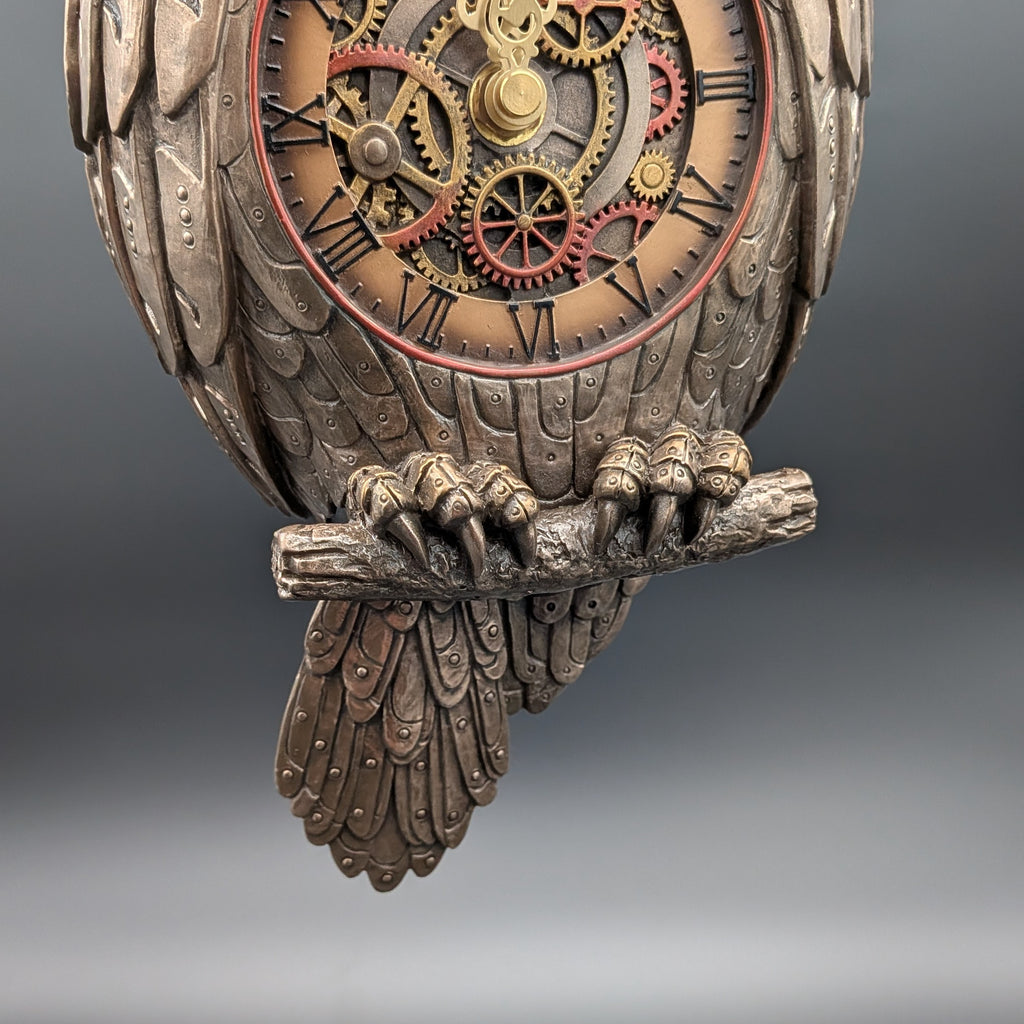 Steampunk owl wall clock featuring a detailed owl body with textured feathers, clawed feet gripping a branch, and an exposed mechanical gear face with Roman numerals and red cog accents.