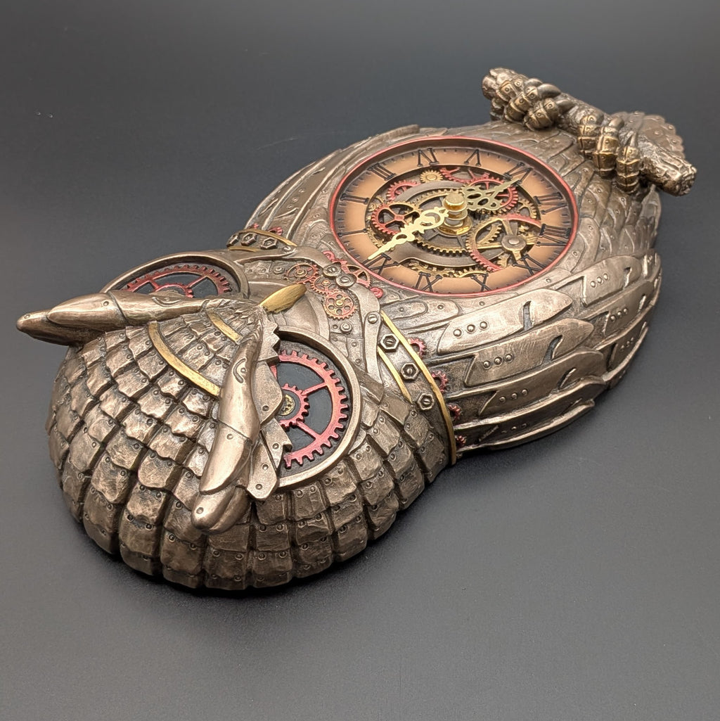 Steampunk owl clock sculpture in metallic bronze and silver tones with intricate gears, red clockwork accents, and a dark gray background.