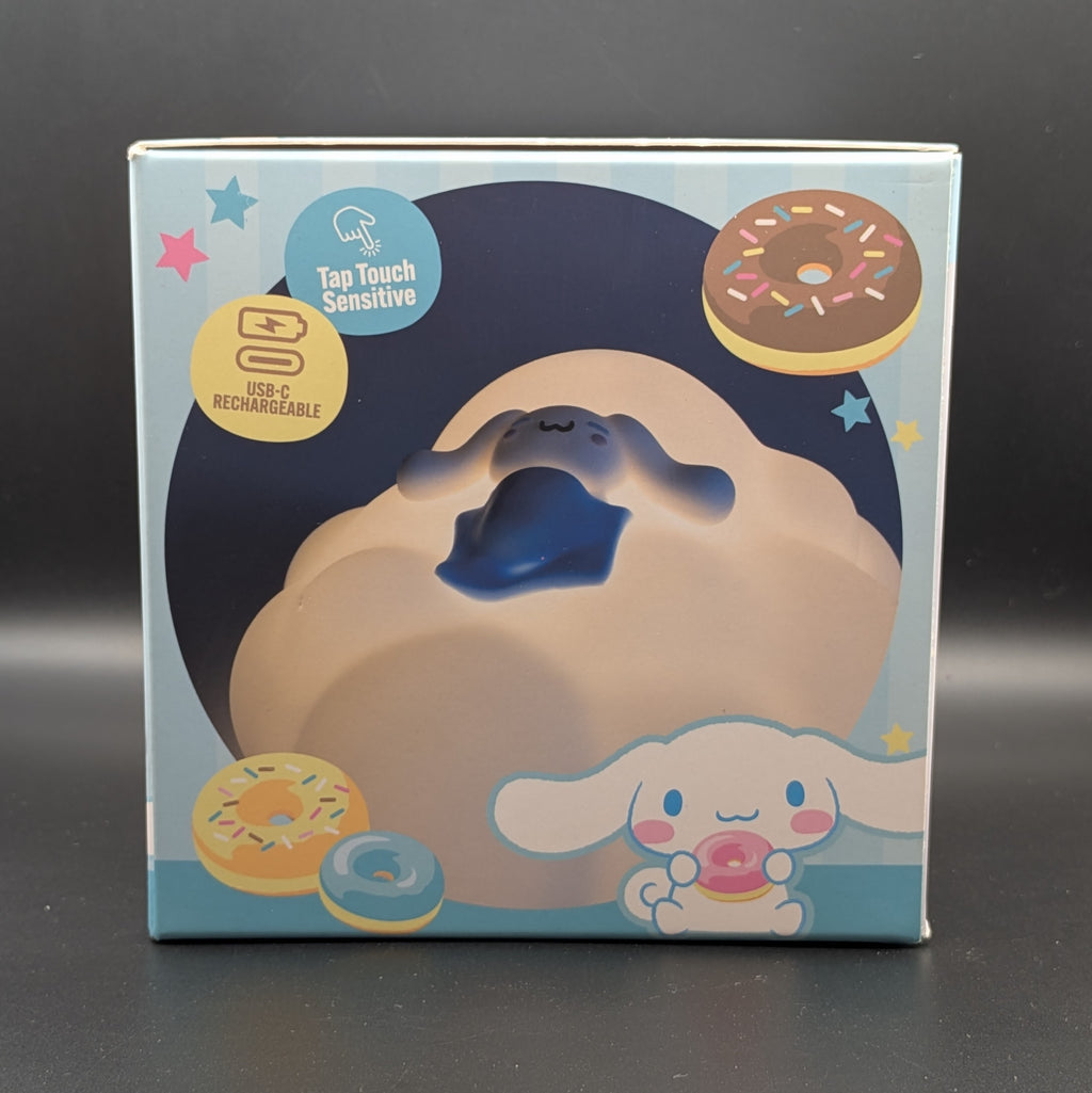 Sanrio Cinnamoroll touch-sensitive lamp in its original retail packaging, featuring a cloud-like body with a sleeping character on top. The box is decorated with donuts and cartoon illustrations.