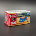 A boxed Tomica Crayon Shinchan toy car, number 169, featuring Crayon Shinchan and Takara Tomy branding on the packaging, photographed on a dark gray surface.