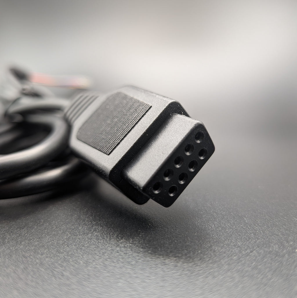 A close-up shot of a black multi-pin electrical connector on a cable, resting on a textured gray surface with a blurred background.