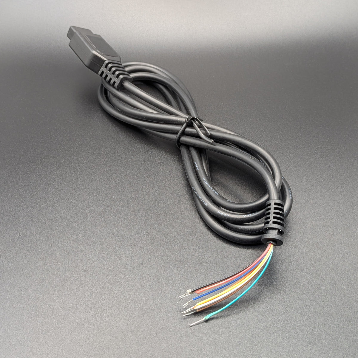 A shot of a black multi-pin electrical connector cable, resting on a textured gray surface with 9 coloured tails.