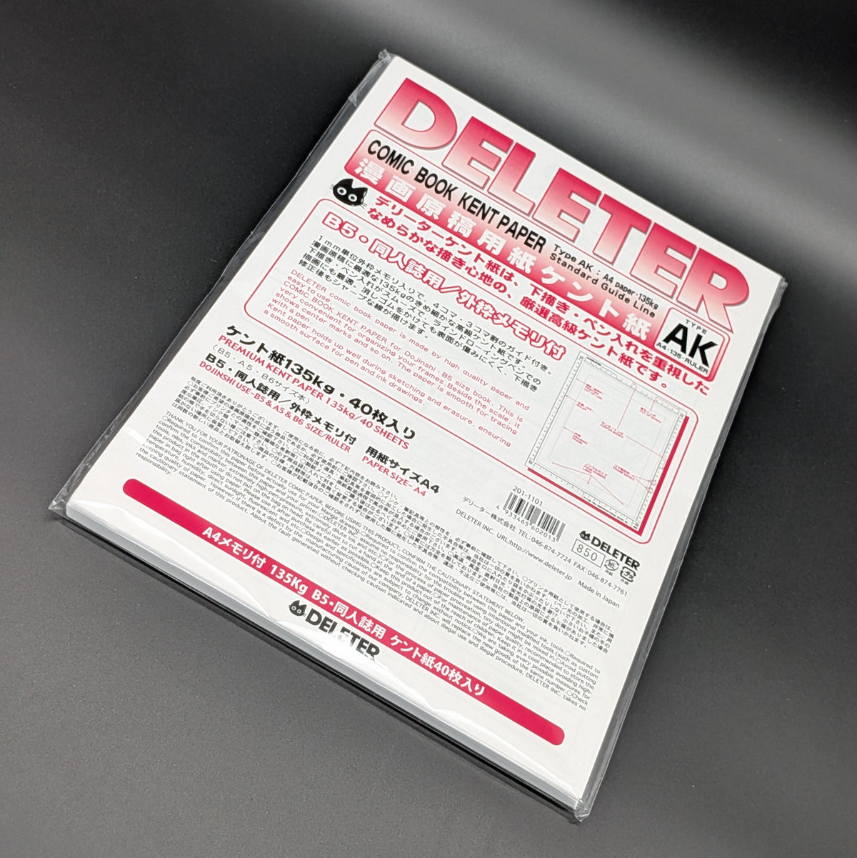 A sealed package of Deliter Comic Book Kent Paper, Type AK, containing 40 sheets of 135g premium paper. The packaging is white with bold pink and black text, the paper is leaning dramatically to the right and photographed on a grey background.
