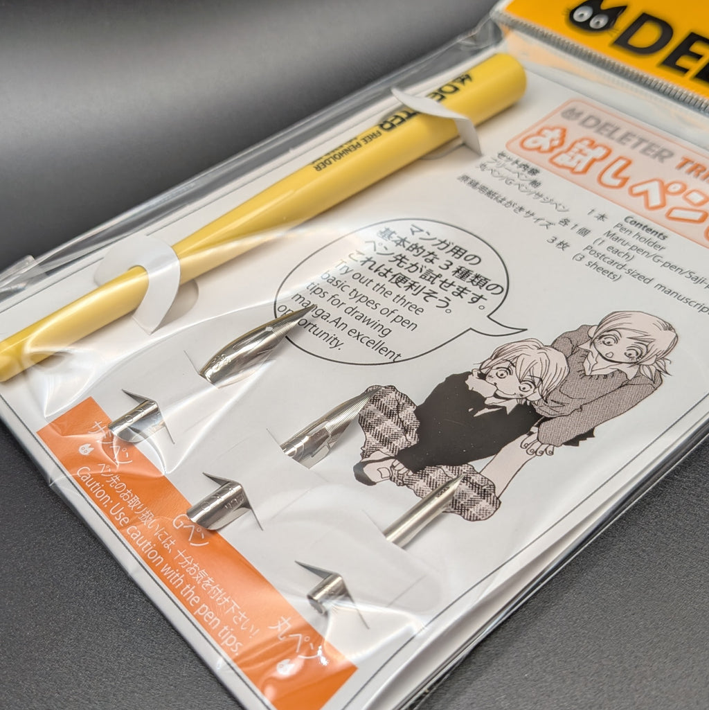 DELETER Trial Pen Set in its original retail packaging, featuring a yellow pen, 3 pen nibs, manuscript paper, with a white and orange card insert.  The picture shows a close up of the nibs included, taken on a black background.