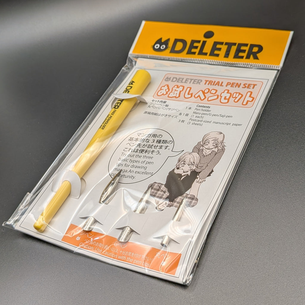 The DELETER Trial Pen Set in its original retail packaging, featuring a yellow pen, 3 pen nibs, manuscript paper, with a white and orange card insert.  The picture shows the item at a 3/4 view angle, leaning to the right, taken on a black background.