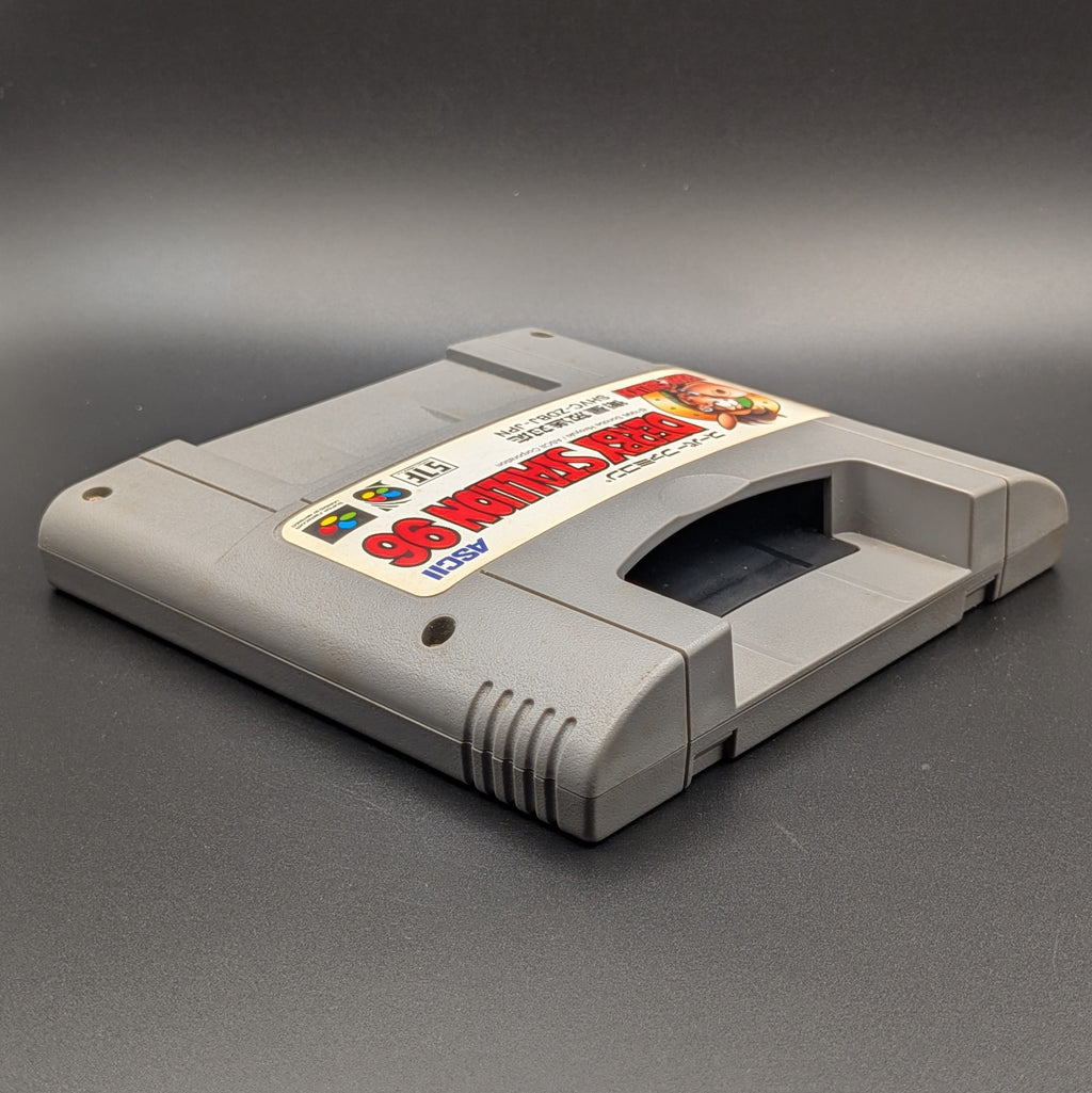 Derby Stallion 96 video game cartridge for Nintendo's Super Famicom (SFC) Entertainment System, shown laying on its back with the label facing upwards. Showing the right hand side and top slot. It sits on a dark grey background.