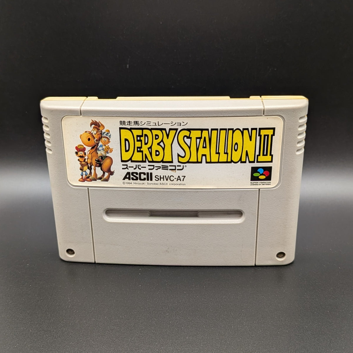 Derby Stallion 2  video game cartridge for Nintendo's Super Famicom (SFC) Entertainment System, shown standing up and facing forward on a dark grey background.
