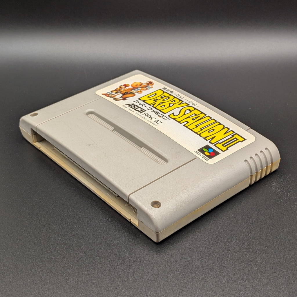Derby Stallion 2 video game cartridge for Nintendo's Super Famicom (SFC) Entertainment System, shown laying on its back with the label facing upwards. Showing the right hand side and bottom slot. It sits on a dark grey background.