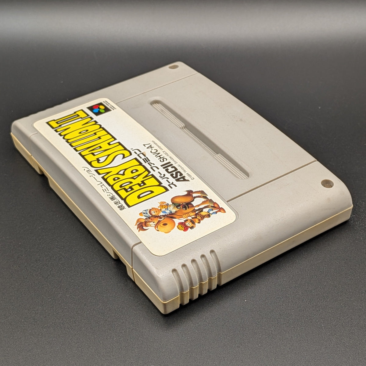 Derby Stallion 2 video game cartridge for Nintendo's Super Famicom (SFC) Entertainment System, shown laying on its back with the label facing upwards. Showing the left hand side and top edge. It sits on a dark grey background.