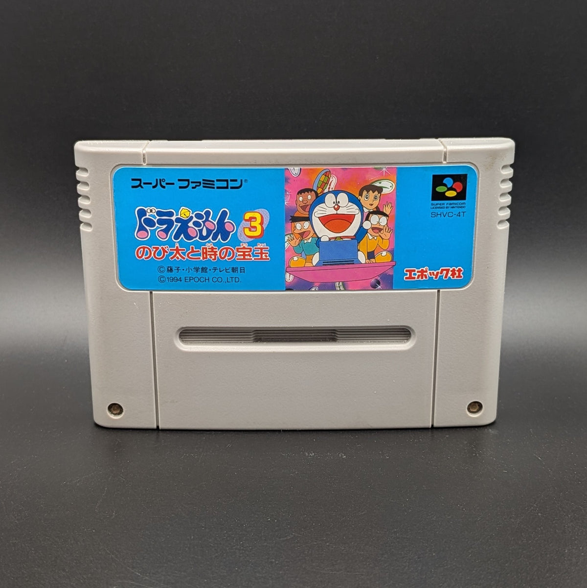 Doraemon 3 video game cartridge for Nintendo's Super Famicom (SFC) Entertainment System, shown standing up and facing forward on a dark grey background.