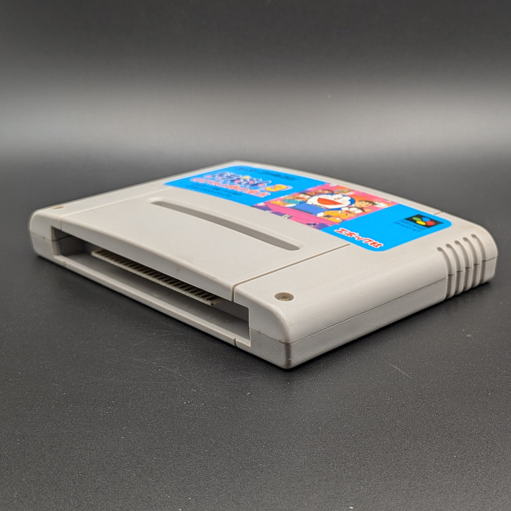 Doraemon 3 video game cartridge for Nintendo's Super Famicom (SFC) Entertainment System, shown laying on its back with the label facing upwards. Showing the right hand side and bottom slot. It sits on a dark grey background. 