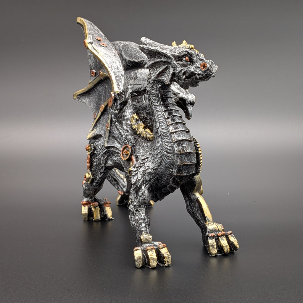 A detailed fantasy dragon figurine with a dark metallic black and silver body, featuring gold accents on its claws, wings, and armor, standing on a dark gray surface against a gradient gray background.