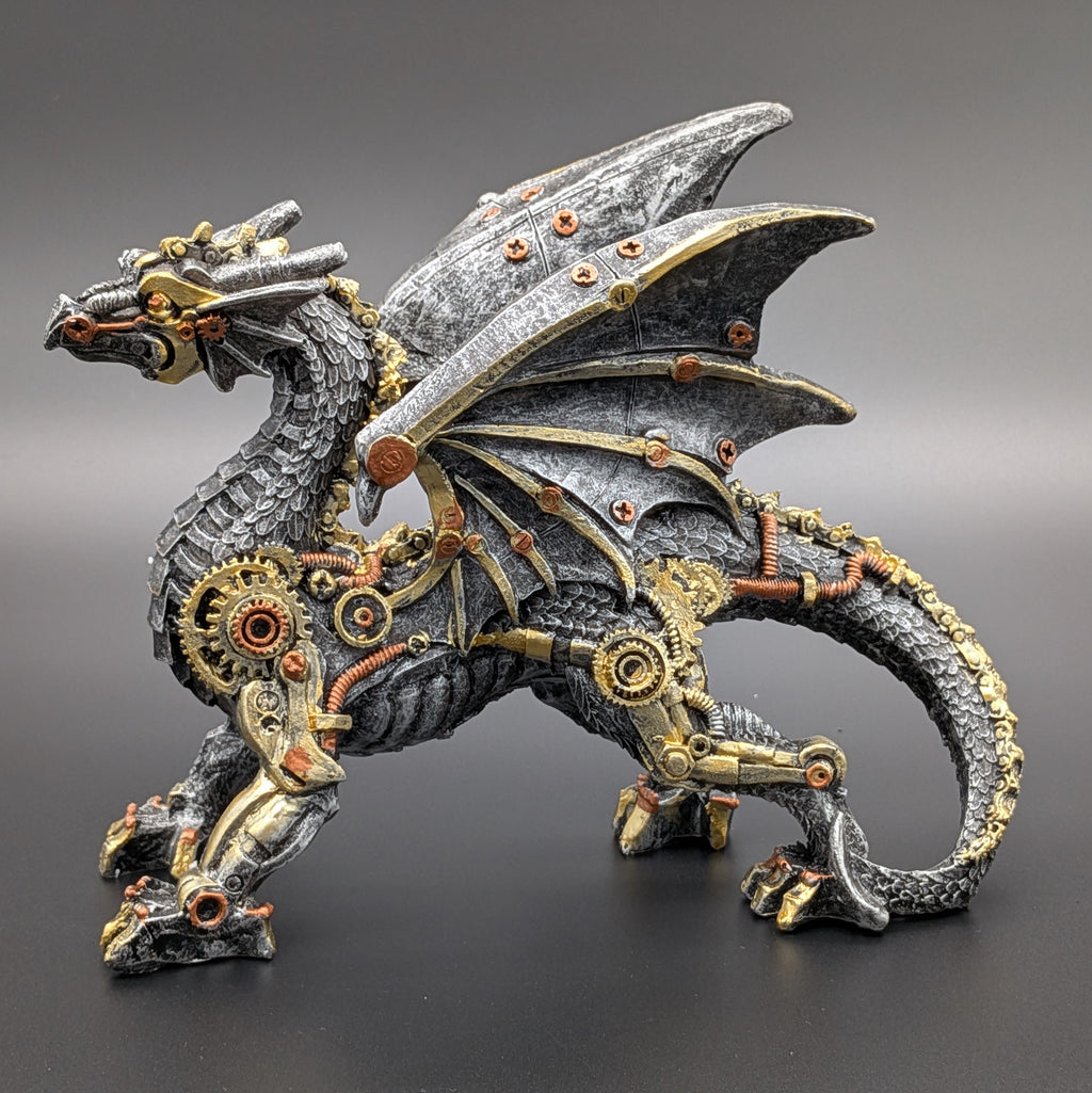 A steampunk-style fantasy dragon figurine with metallic gray scales, gold gears, and copper mechanical details, standing on a dark gray surface against a gradient gray background.
