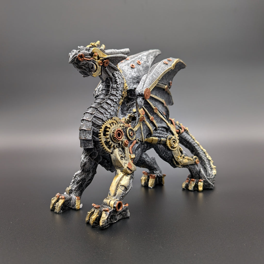 A steampunk-style fantasy dragon figurine with metallic gray scales, gold gears, and copper/brass mechanical details, standing on a dark gray surface against a gradient gray background.