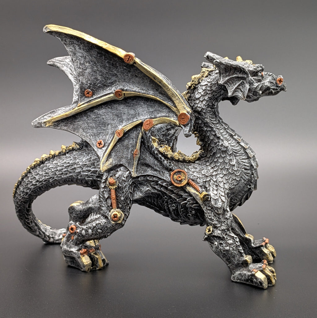 A detailed fantasy dragon figurine in a dynamic pose, featuring a textured dark gray and black scale pattern with metallic gold accents on its wings, claws, and joints, set against a dark gray gradient background.
