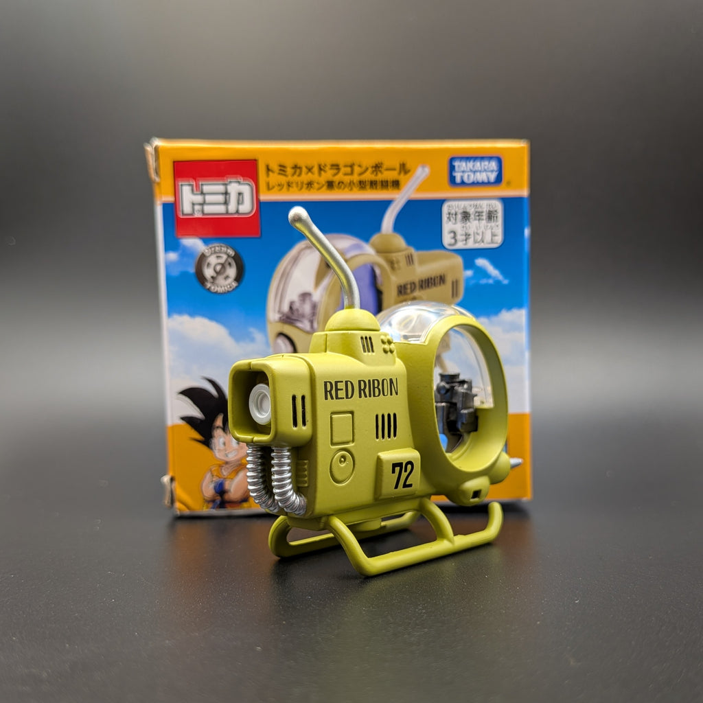 A green Dragon Ball toy Helicopter model labeled 'RED RIBBON 72' displayed in front of its original packaging box on a dark gray surface.