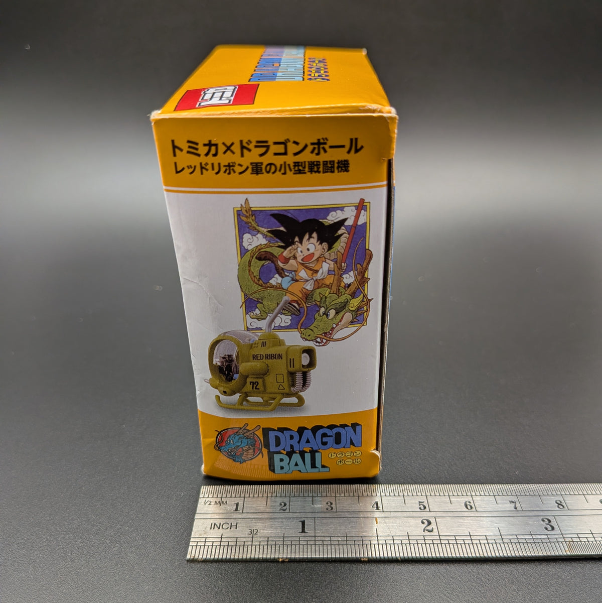 Dragon Ball Z collectible toy box in Japanese, featuring Goku and the Dragon Ball, shown next to a metal ruler on a gray background.