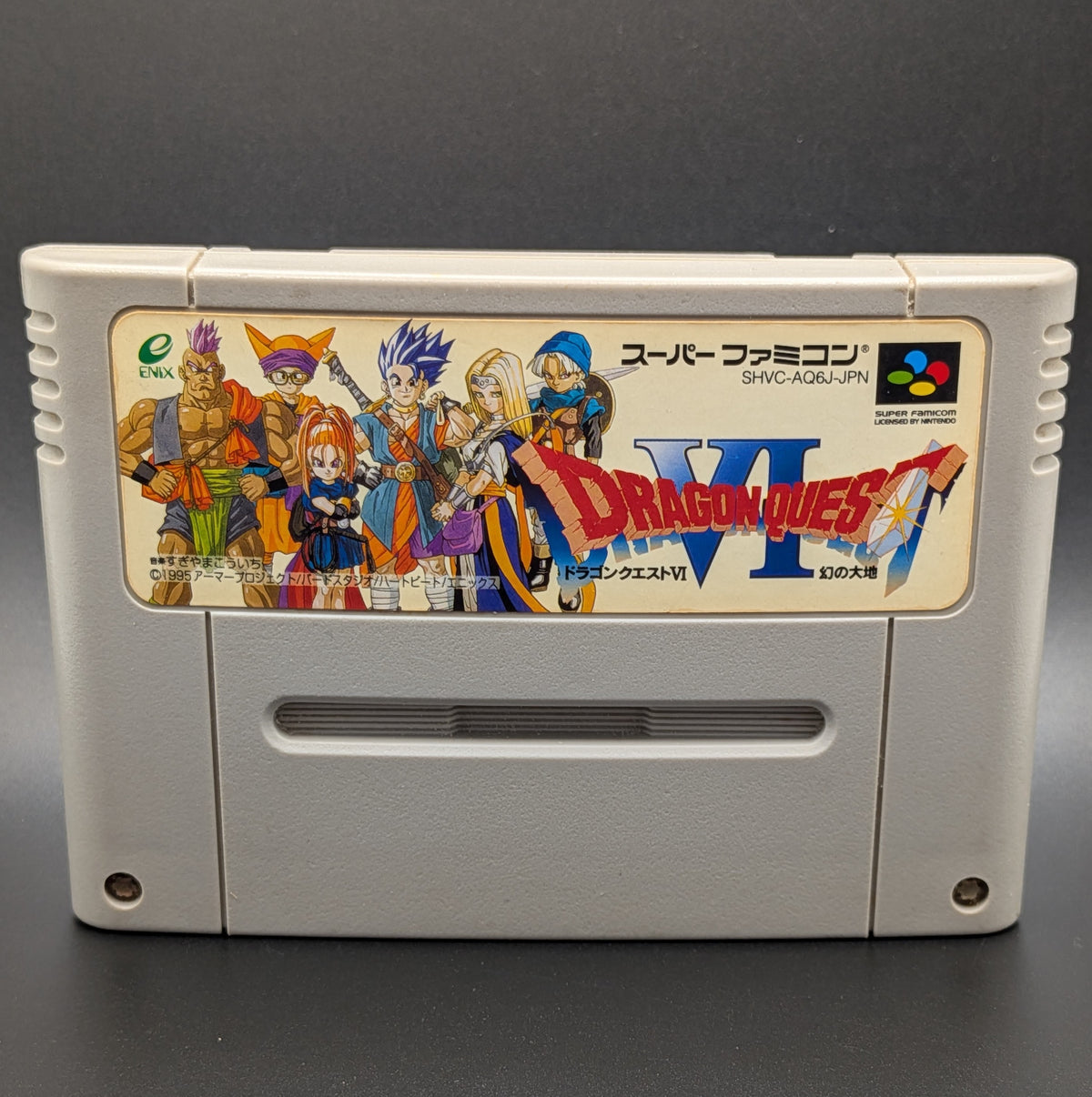 A close up of Dragon Quest 6 video game cartridge for Nintendo's Super Famicom (SFC) Entertainment System, shown standing up and facing forward on a dark grey background.