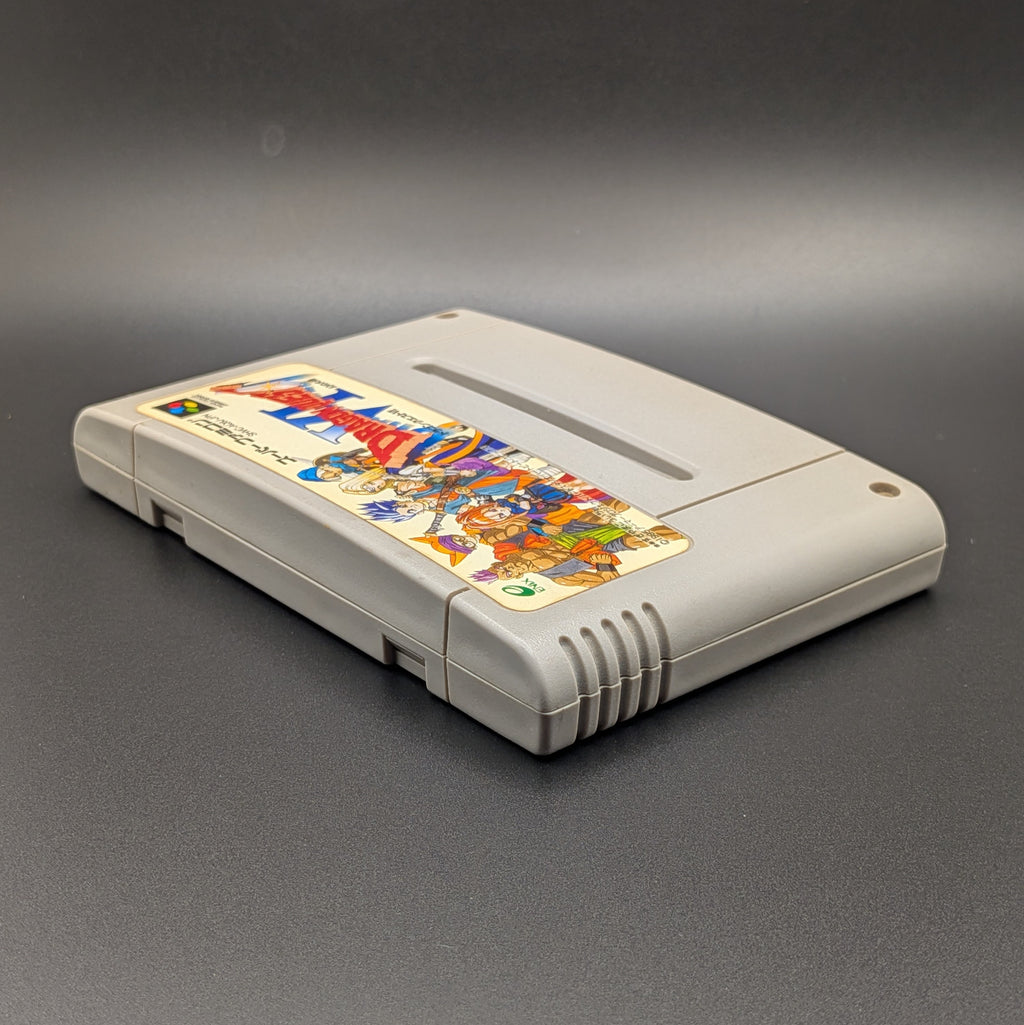Dragon Quest 6 video game cartridge for Nintendo's Super Famicom (SFC) Entertainment System, shown laying on its back with the label facing upwards. Showing the left hand side and top edge. It sits on a dark grey background.