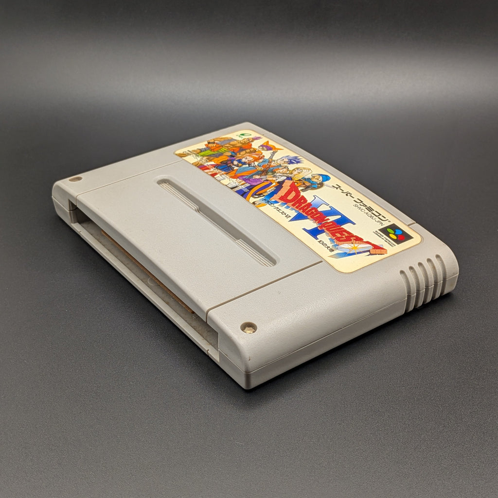 Dragon Quest 6 video game cartridge for Nintendo's Super Famicom (SFC) Entertainment System, shown laying on its back with the label facing upwards. Showing the right hand side and bottom slot. It sits on a dark grey background.