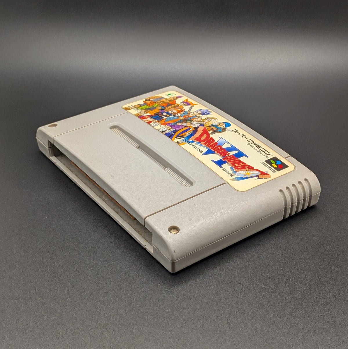 Dragon Quest 6 video game cartridge for Nintendo's Super Famicom (SFC) Entertainment System, shown laying on its back with the label facing upwards. Showing the right hand side and bottom slot. It sits on a dark grey background.