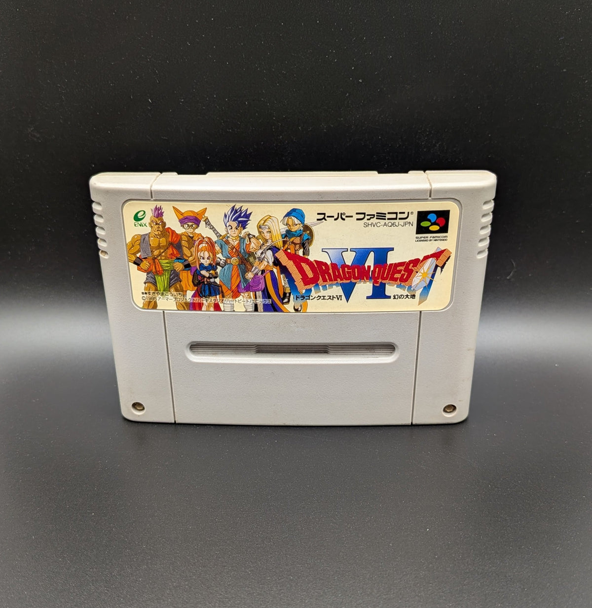 Dragon Quest VI video game cartridge for Nintendo's Super Famicom (SFC) Entertainment System, shown standing up and facing forwards on a dark grey background.