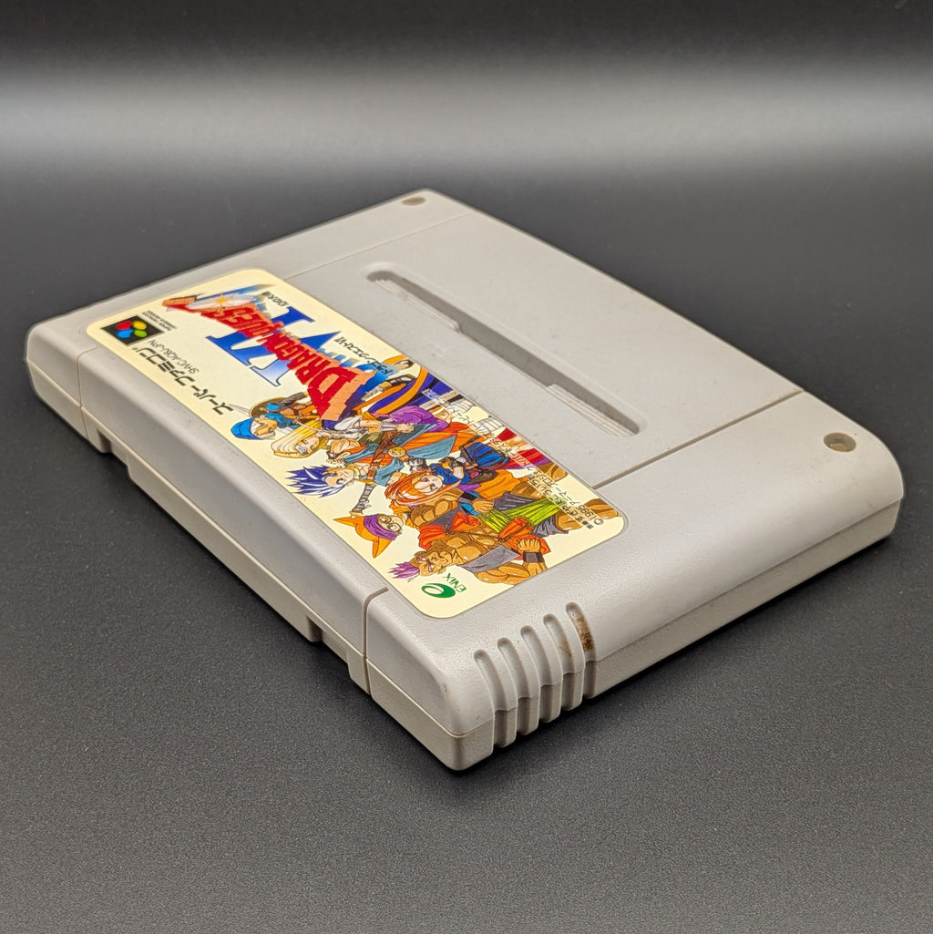 Dragon Quest VI video game cartridge for Nintendo's Super Famicom (SFC) Entertainment System, shown laying on its back with the label facing upwards. Showing the left hand side and top edge. It sits on a dark grey background.