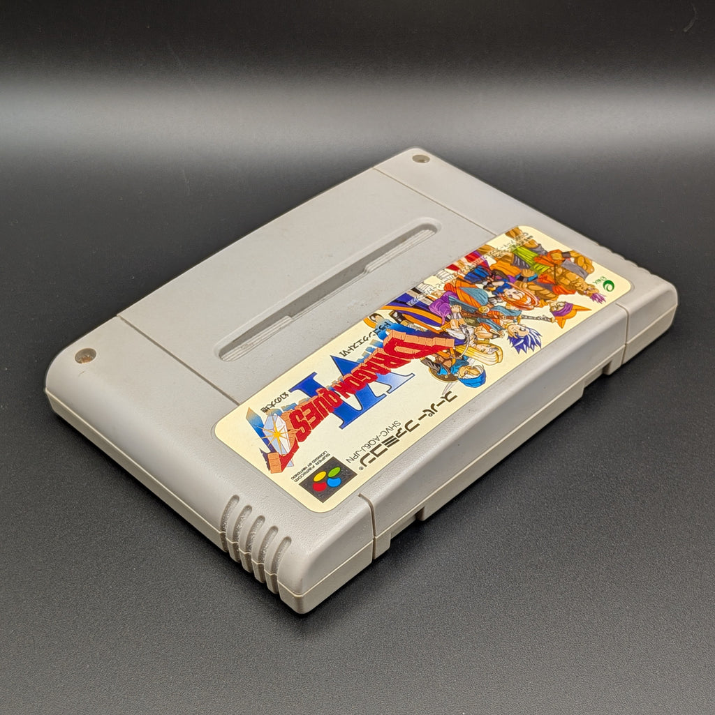 Dragon Quest VI video game cartridge for Nintendo's Super Famicom (SFC) Entertainment System, shown laying on its back with the label facing upwards. Showing the right hand side and top edge. It sits on a dark grey background.